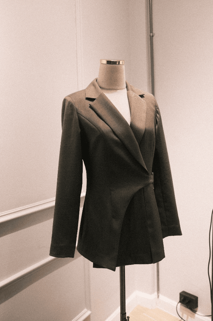 Dark charcoal wrap-style blazer with asymmetric closure on mannequin