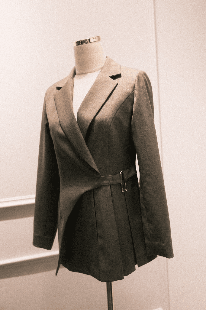 Light taupe wrap blazer with gold buckle and pleated hem on mannequin