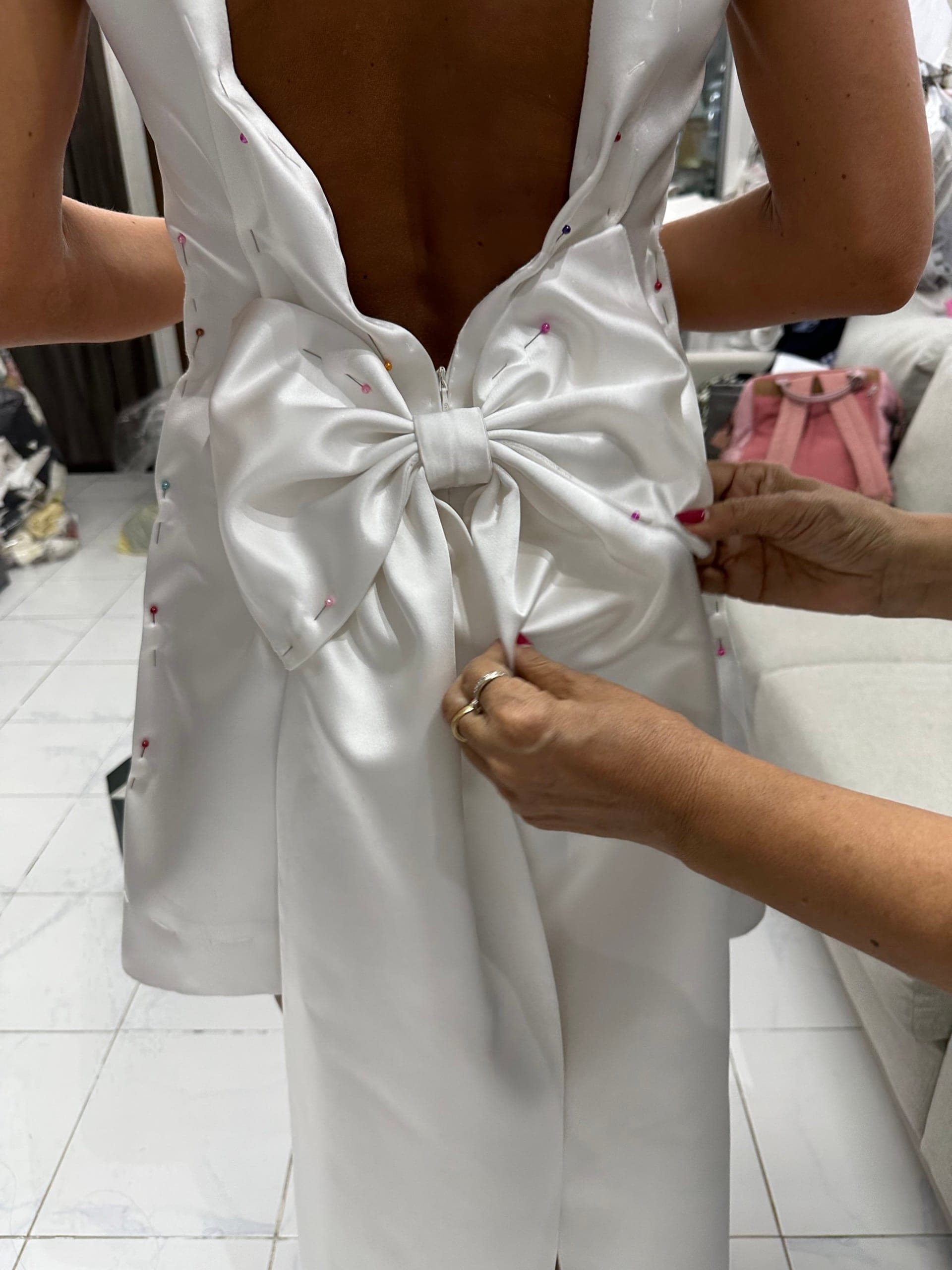 Hands adjusting a pinned satin bow on the back of a wedding dress