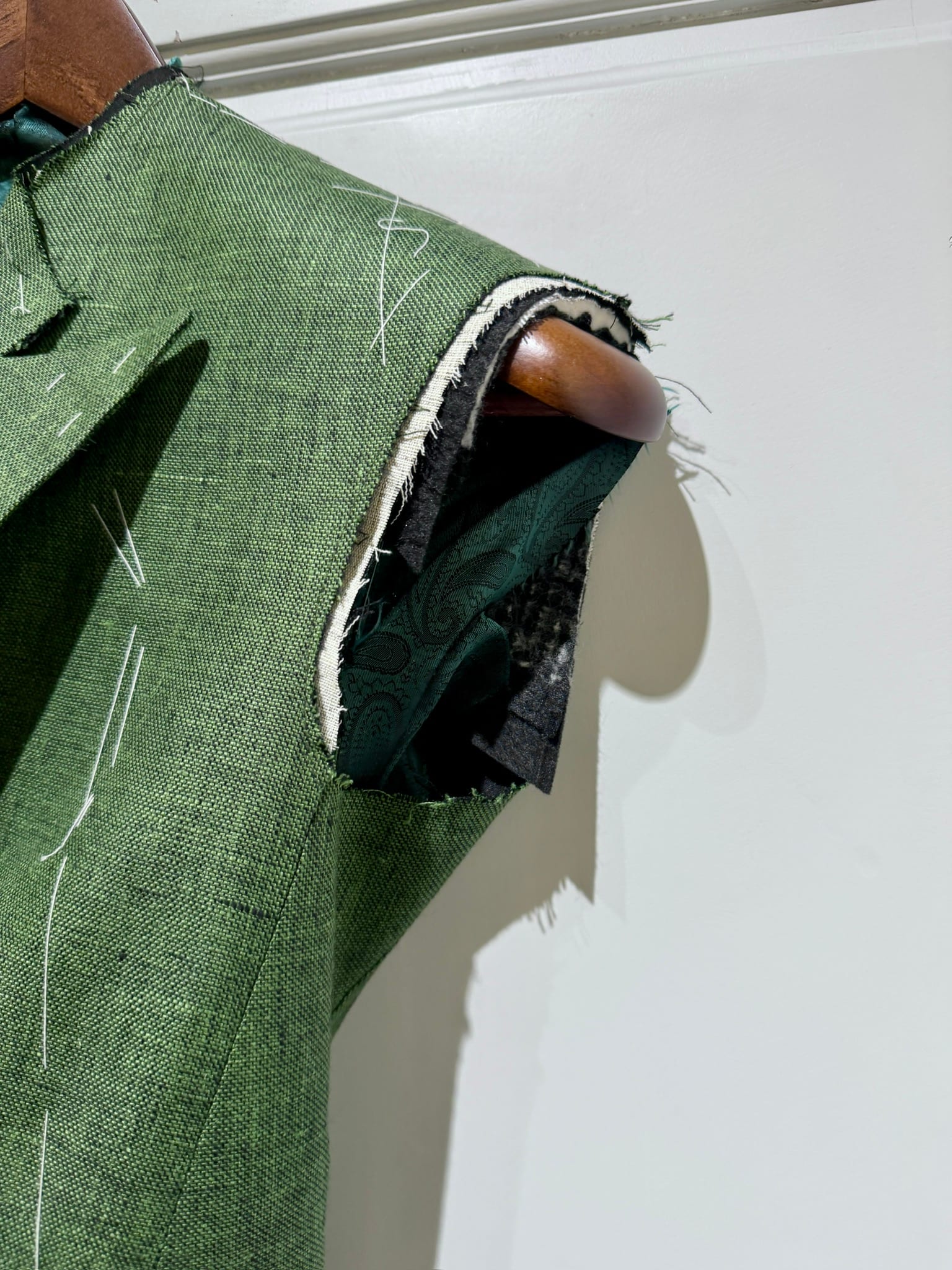 Close-up of basting stitches at the armhole of a green linen jacket during fitting
