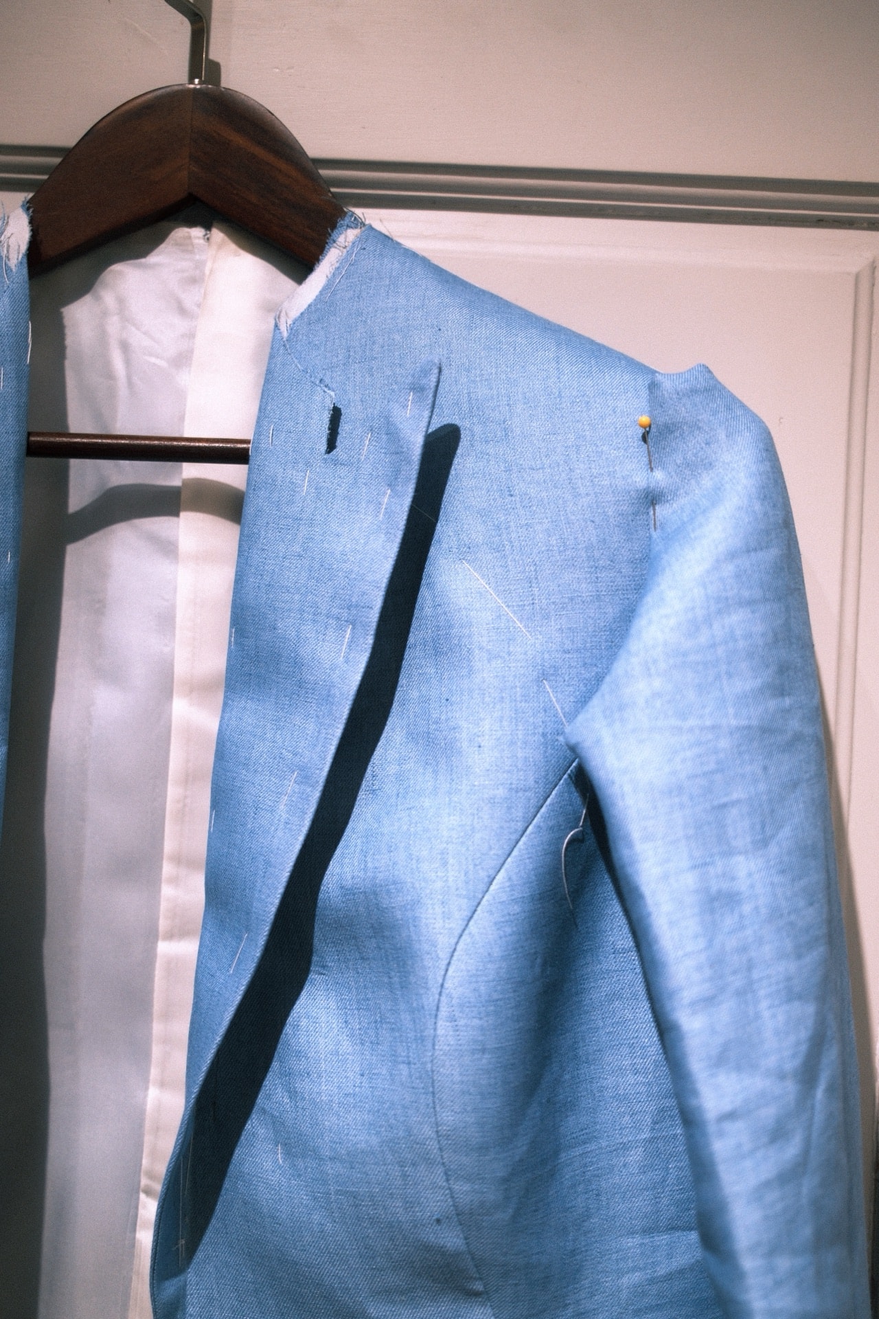 Close-up of basting stitches on the shoulder of a blue linen jacket during fitting