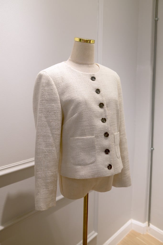 Cream tweed collarless jacket with dark buttons and patch pockets on a mannequin