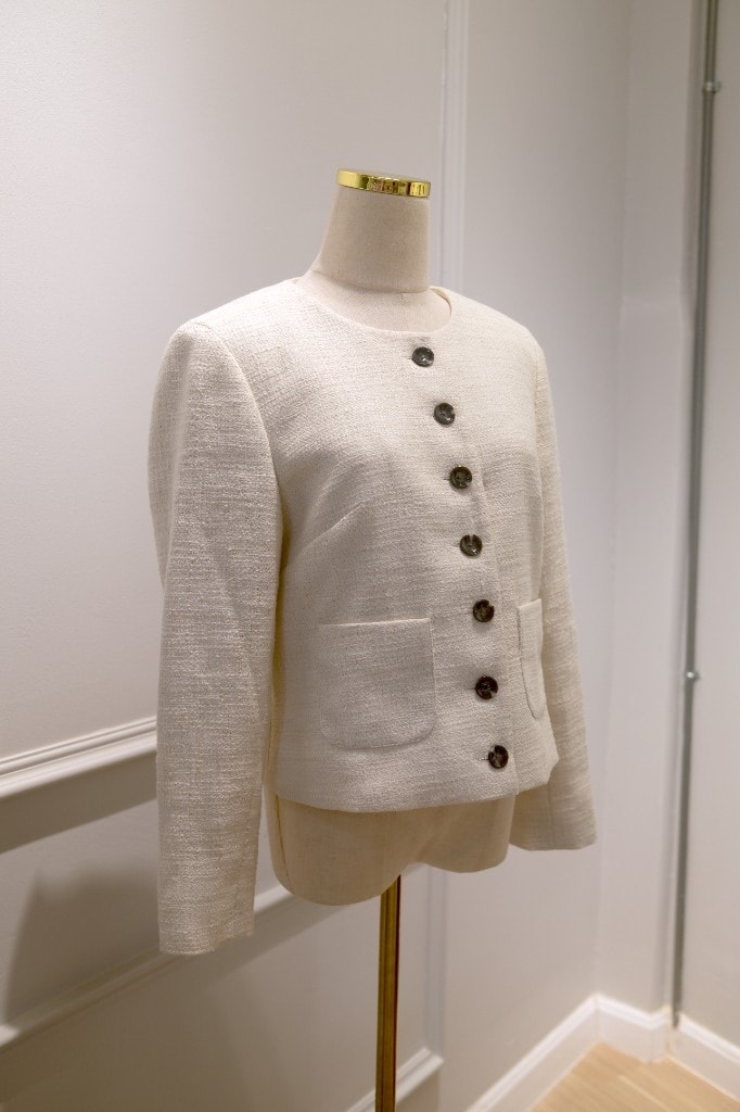 Cream tweed collarless jacket with dark buttons and patch pockets on a mannequin