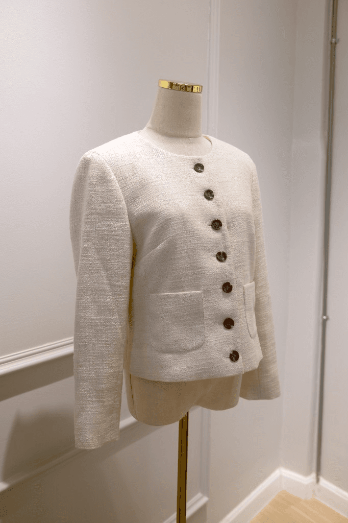 Cream tweed collarless jacket with dark buttons and patch pockets on mannequin