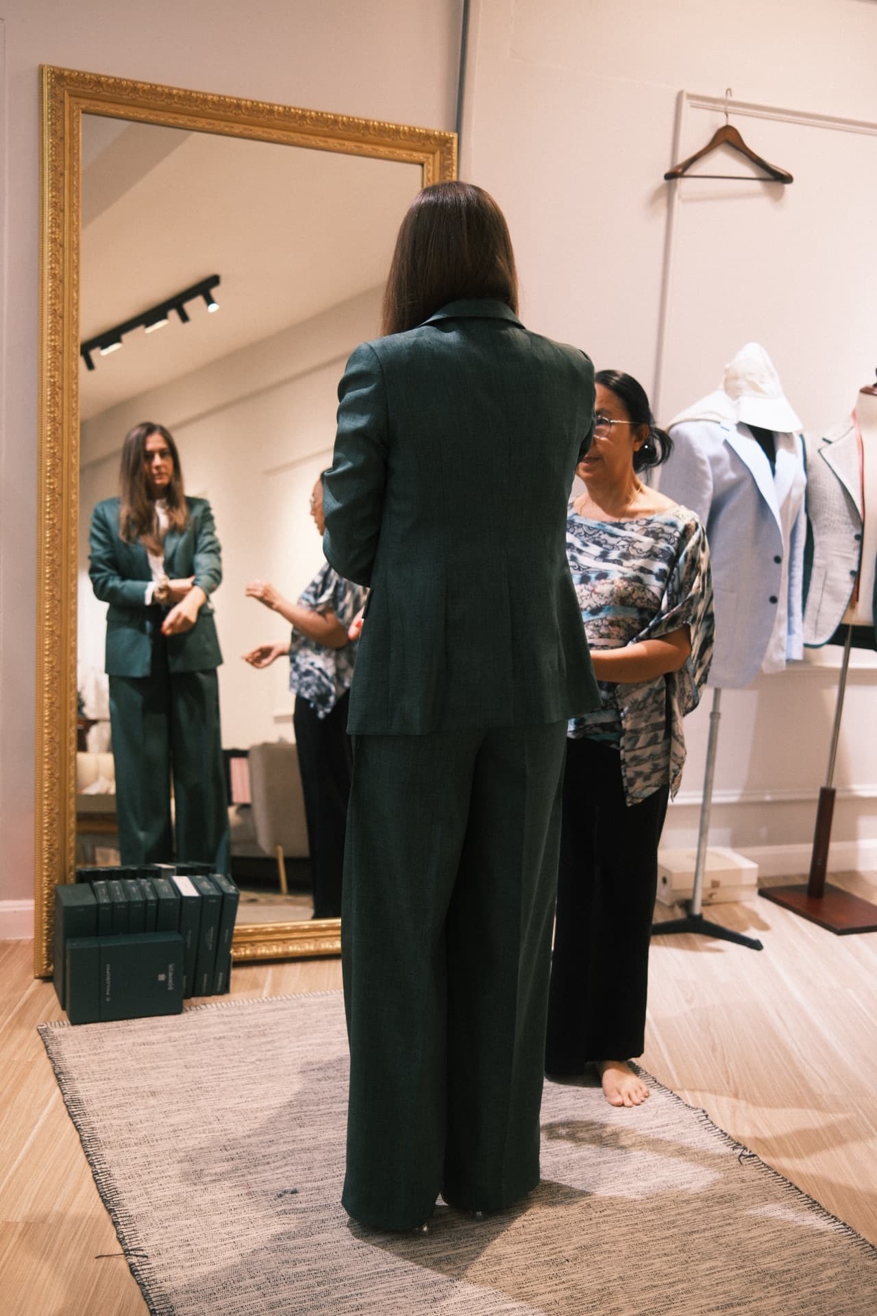 Back view of emerald green women's suit with tailor adjusting the fit at LALEDA