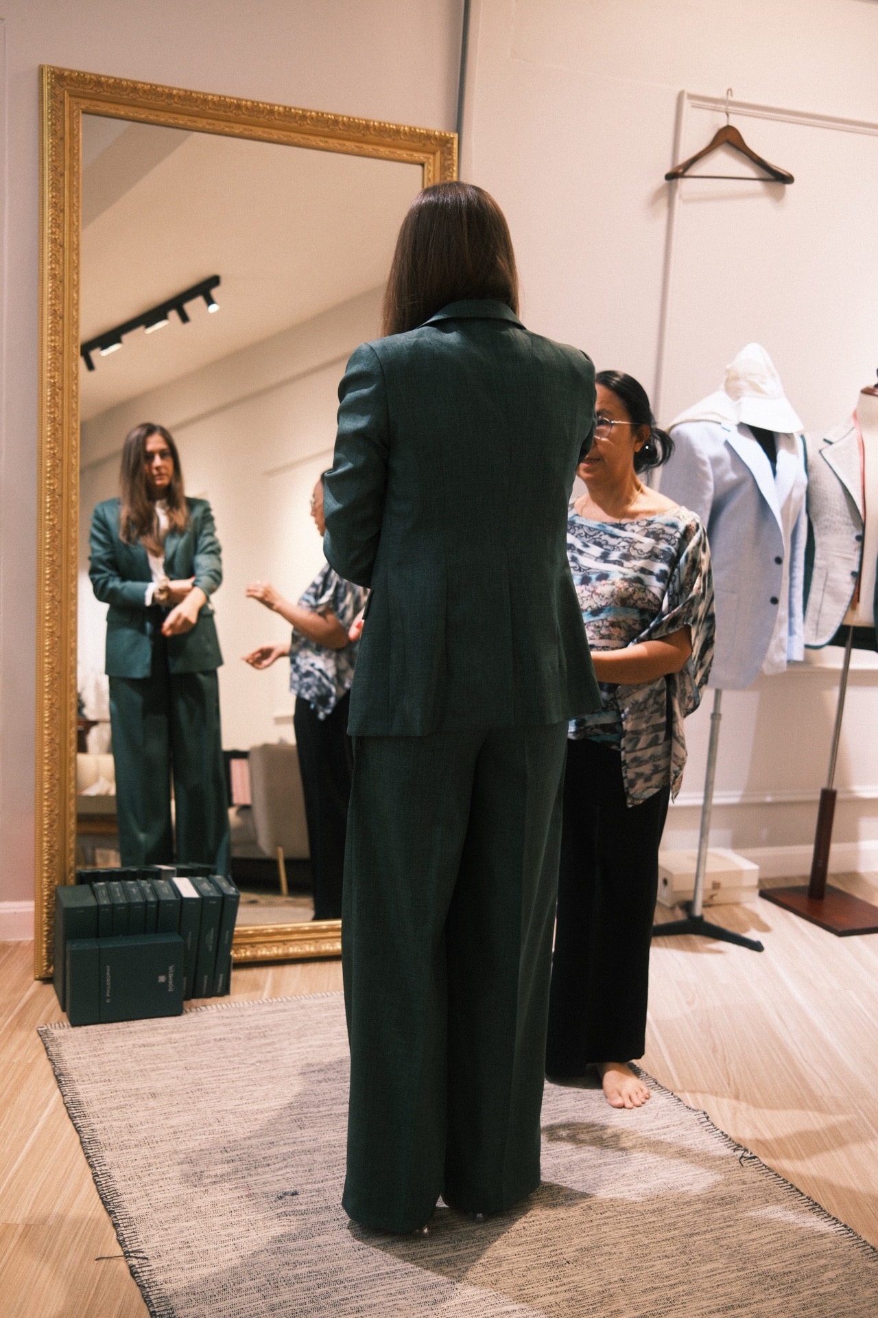 Back view of emerald green women's suit with tailor adjusting the fit at LALEDA