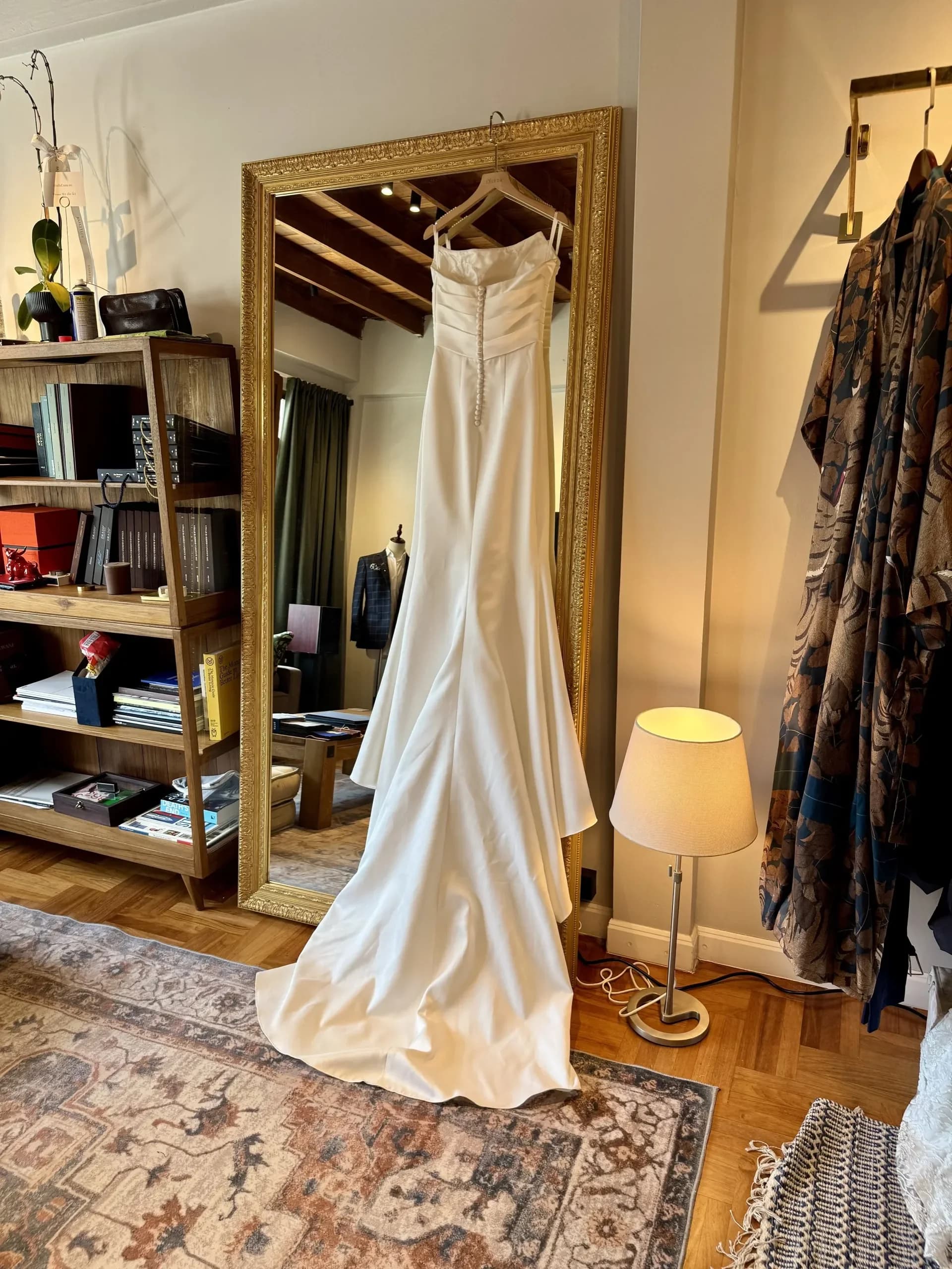 A finished long white wedding dress hanging by the atelier mirror