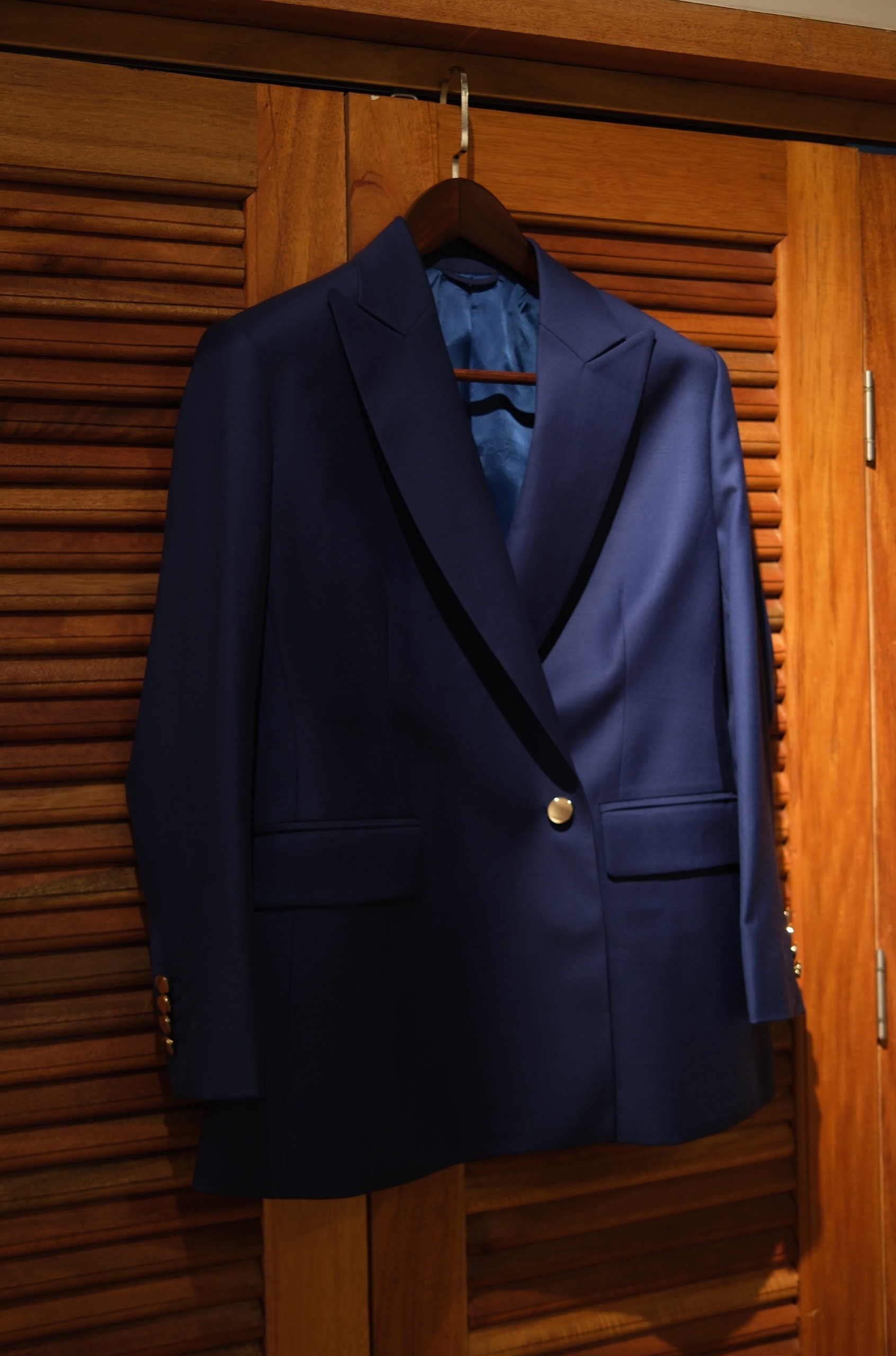Navy double-breasted women's blazer with peak lapels and gold buttons on a hanger