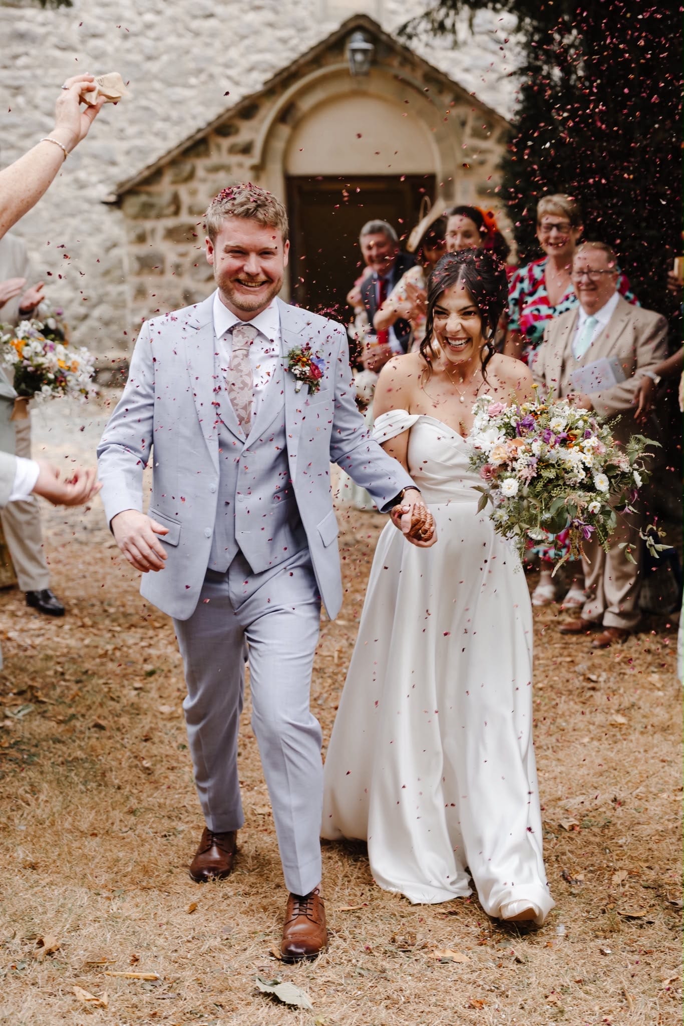 Bride and groom laughing and walking through confetti after their English chapel wedding