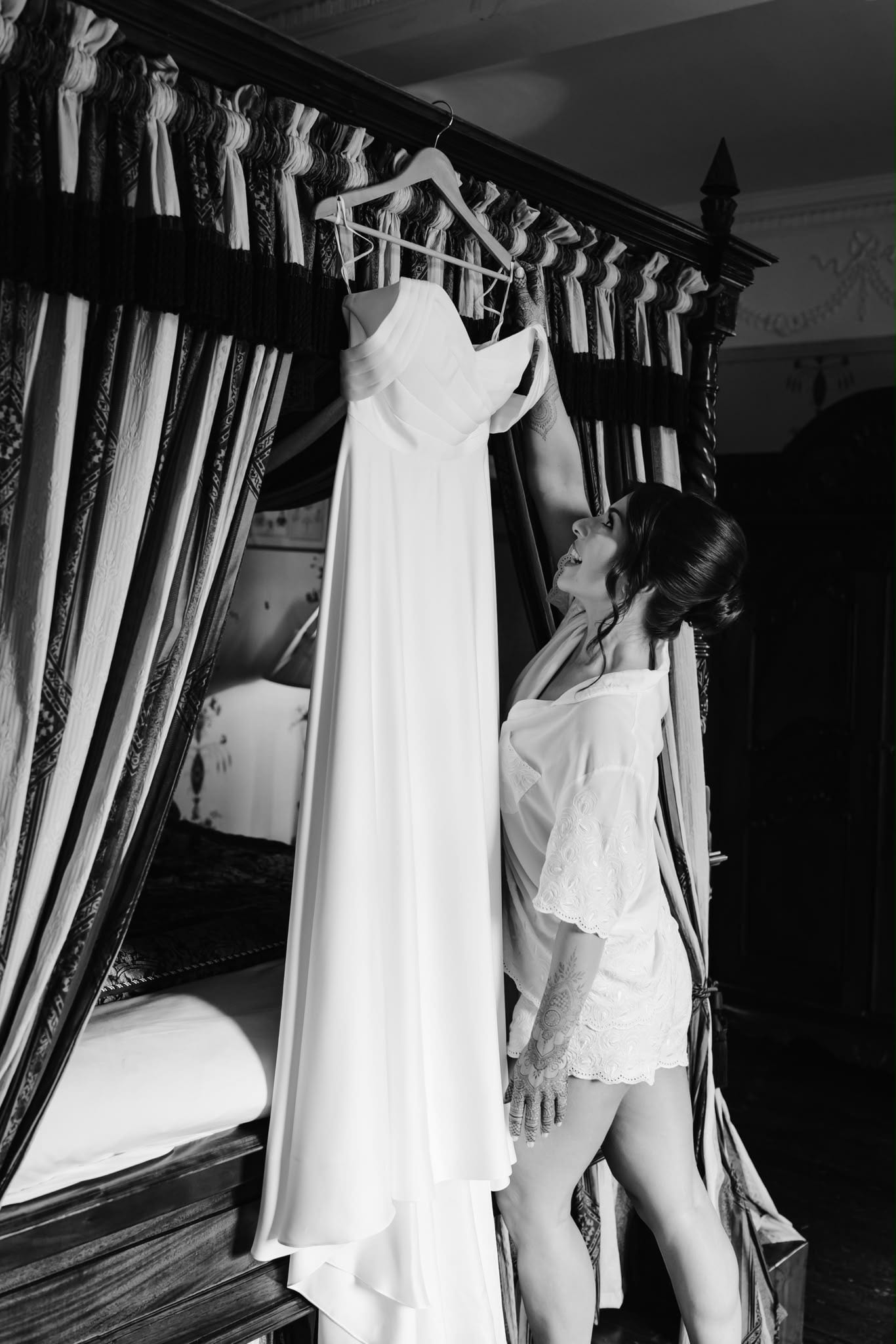 A plain white wedding gown by LALEDA hanging inside a four-poster bed on the morning of the wedding