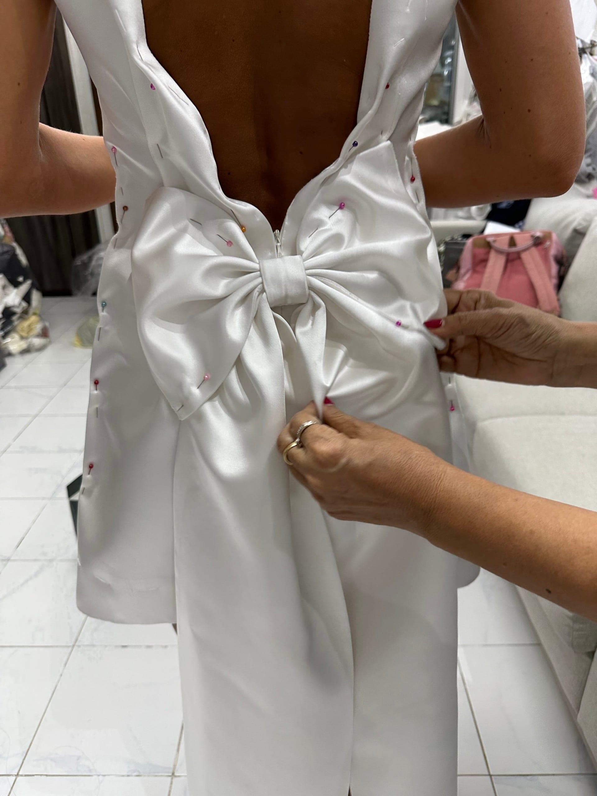 Hands adjusting a pinned satin bow on the back of a wedding dress