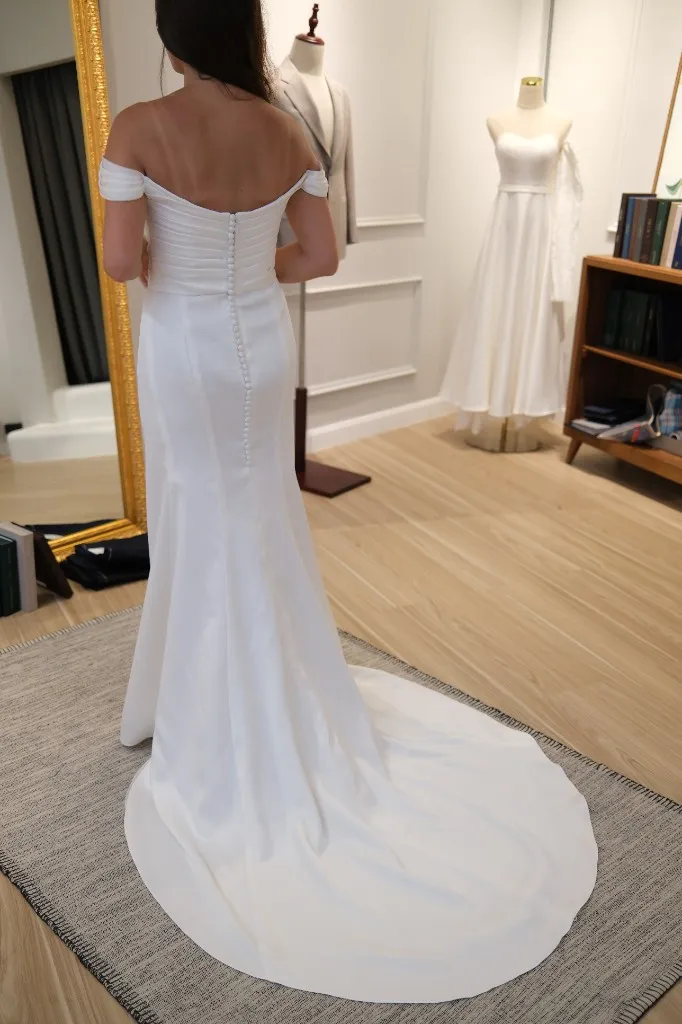 White off-the-shoulder wedding dress with covered buttons and a long train
